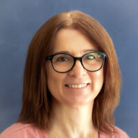 Martina Farova is the office manager and bookkeeper at Listen and Talks early development program for children who are deaf and hard of hearing. Martina is a white woman with brown red hair. She is wearing glasses and a pink shirt.