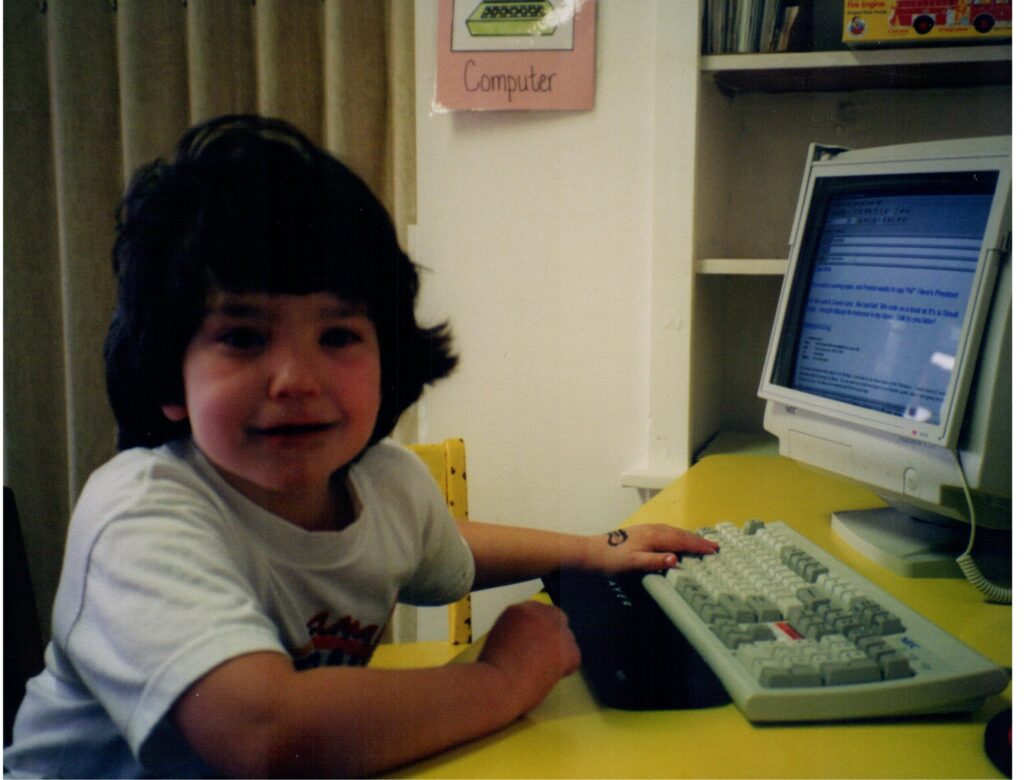 Preston Dwoskin who identifies as hearing impaired is sitting in front of a computer. This photo of Preston was taken when he attended Listen and Talk's preschool for deaf and hard of hearing children.