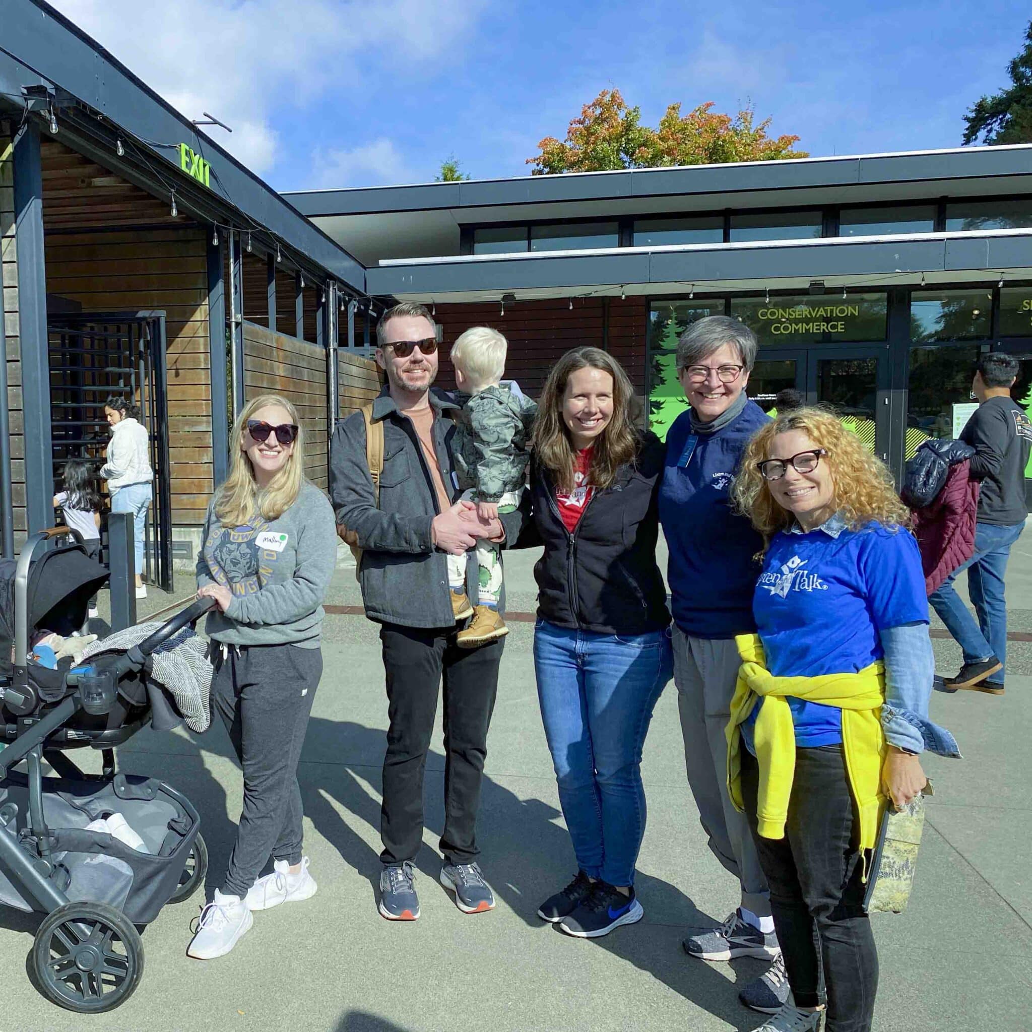 Group of Listen and Talk Staff and Birth to Three providers standing by the Woodland Park Zoo entrance with one of our Birth to Three families and their child.