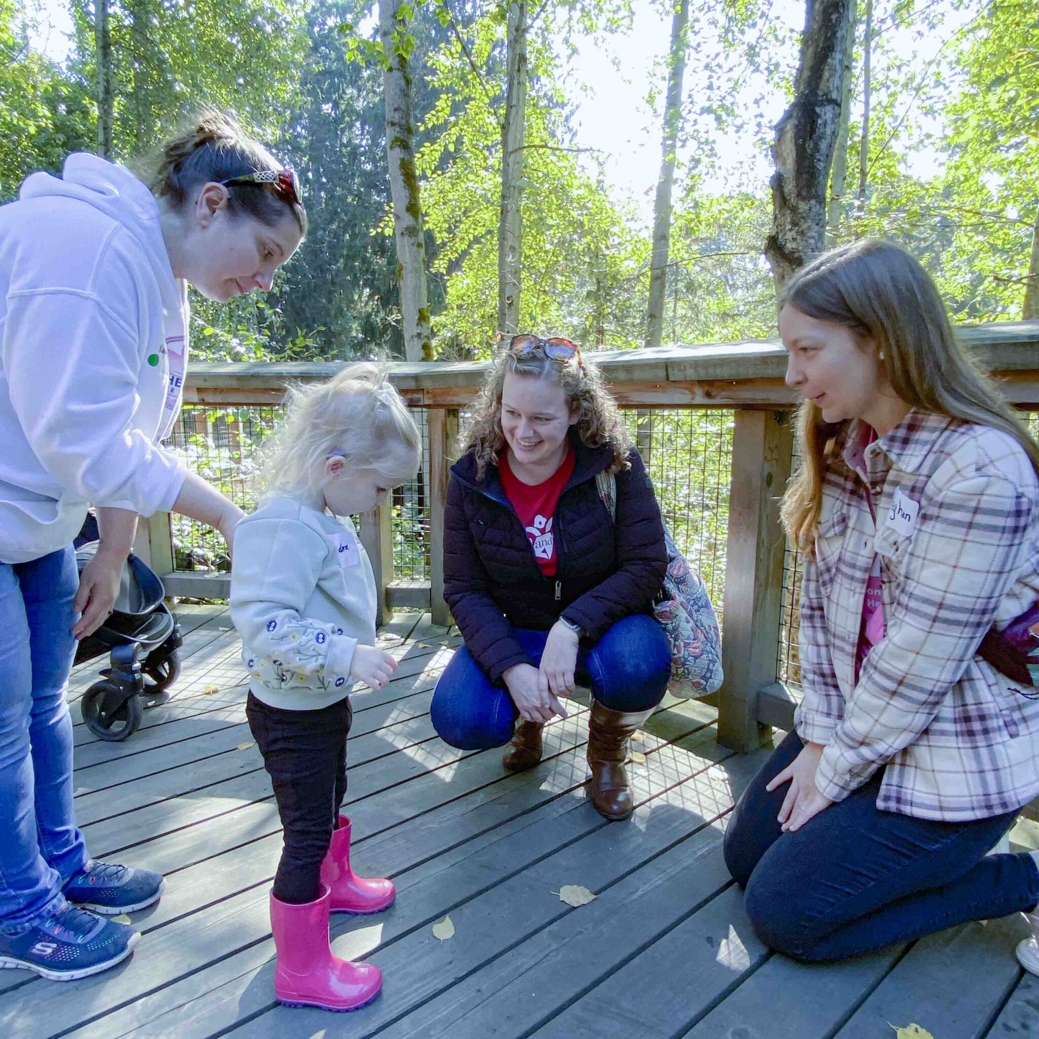 Three adults interact with a deaf child playing on a wooden boardwalk