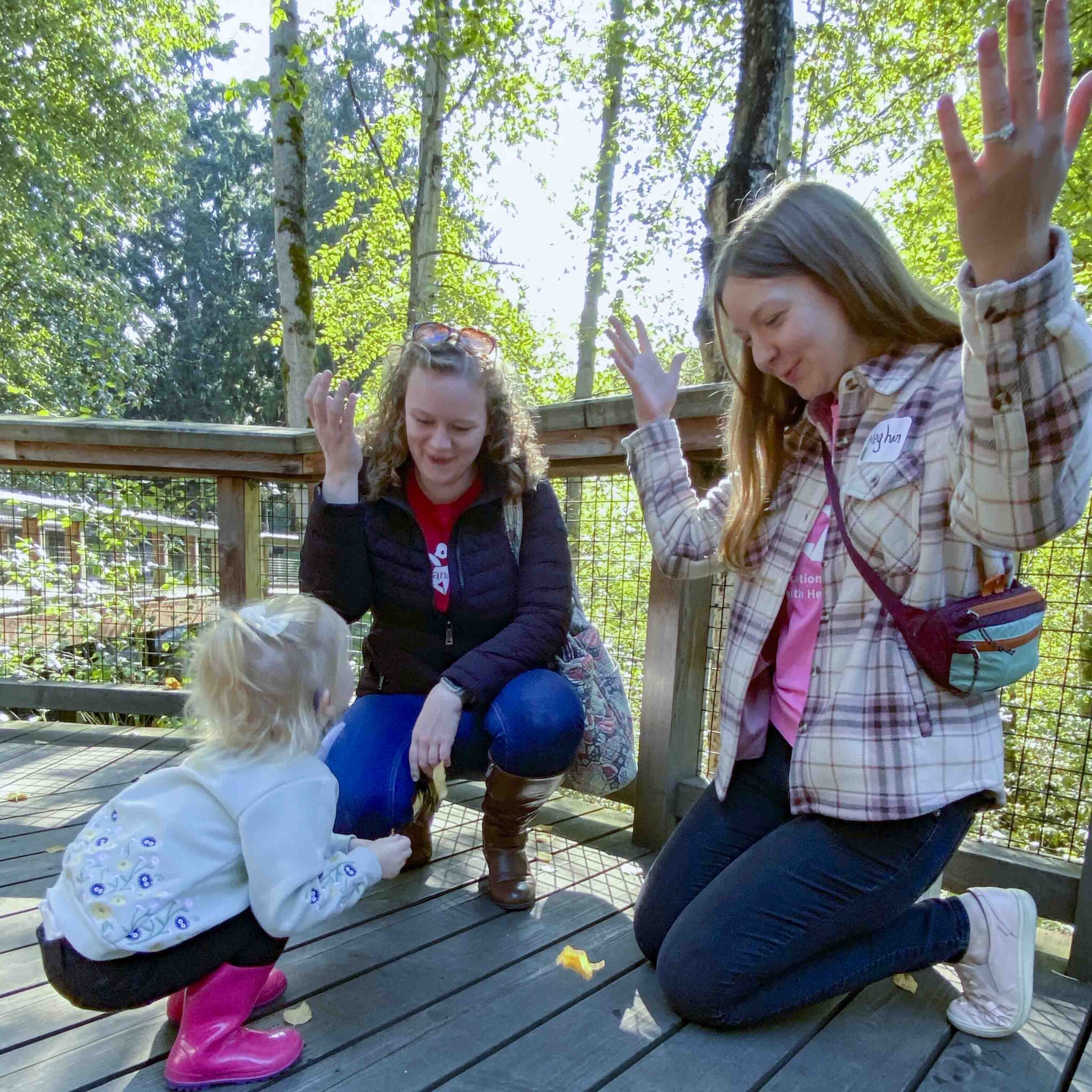 Two adults interact with a deaf child playing on a wooden boardwalk