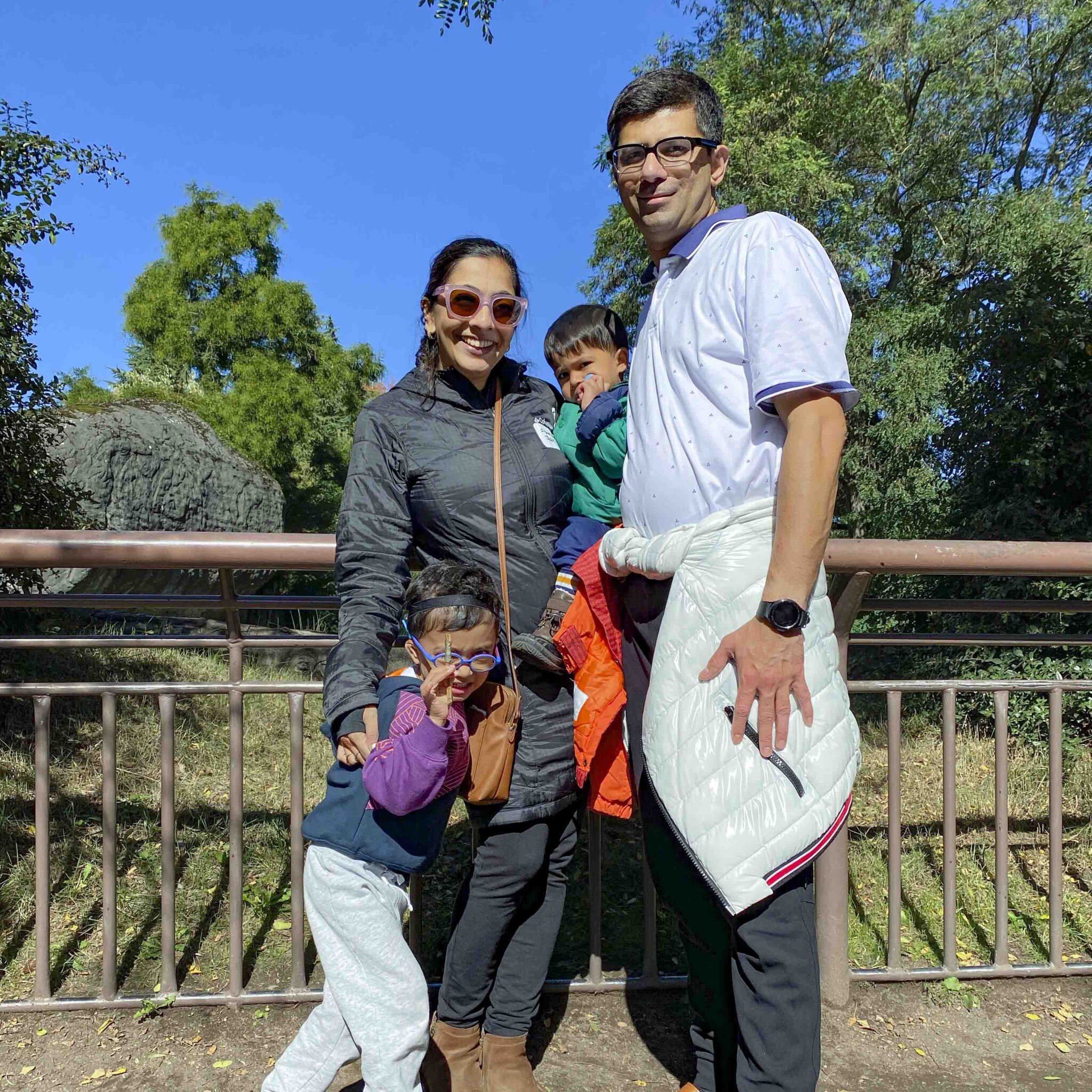 family group photo of two adults and two children standing in front of an empty zoo exhibit.