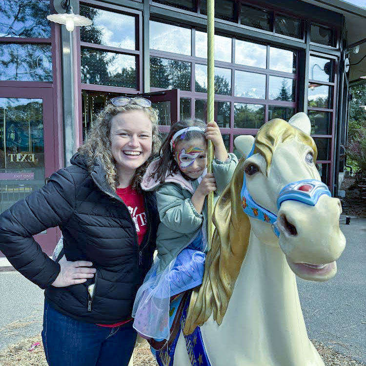 Meghan, one of our B3 providers, stands next to a fake horse ride outside with a child that's sitting on it.
